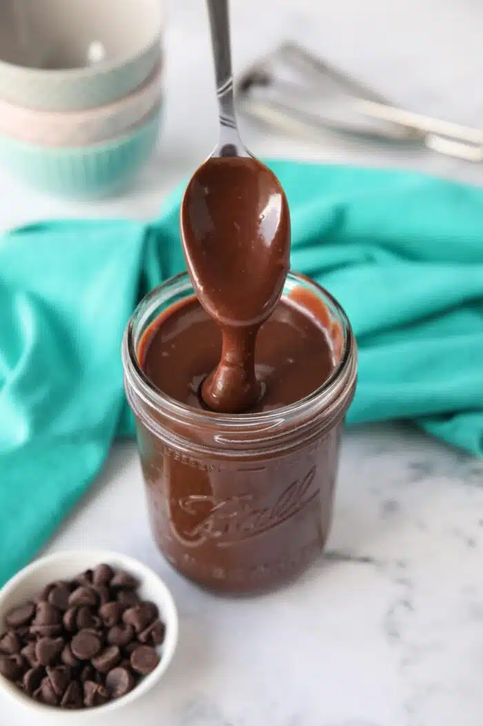 Homemade hot fudge recipe in a mason jar being drizzled with a spoon.