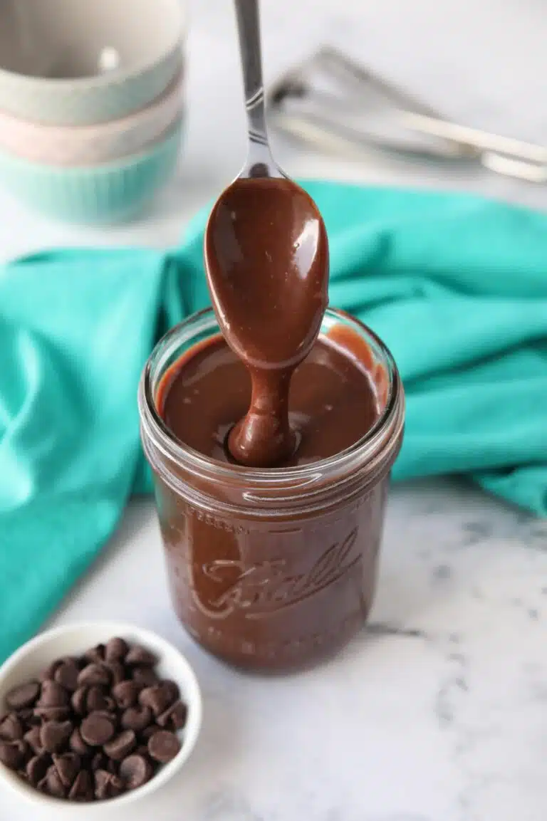 Homemade hot fudge recipe in a mason jar being drizzled with a spoon.