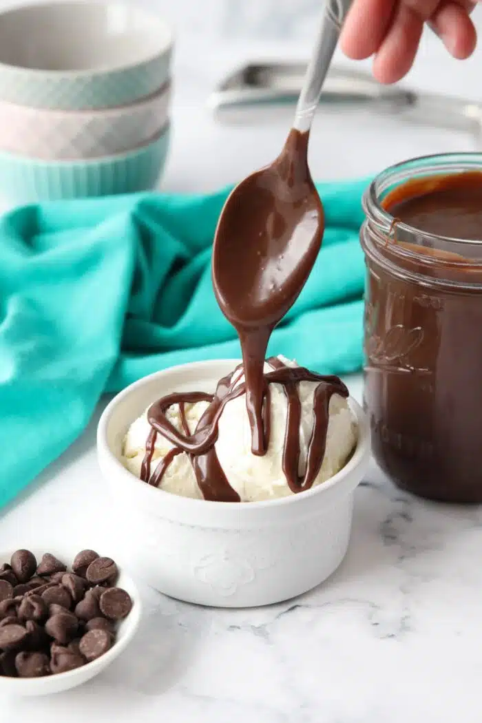 Hot fudge sauce being drizzled over vanilla ice cream with a spoon.