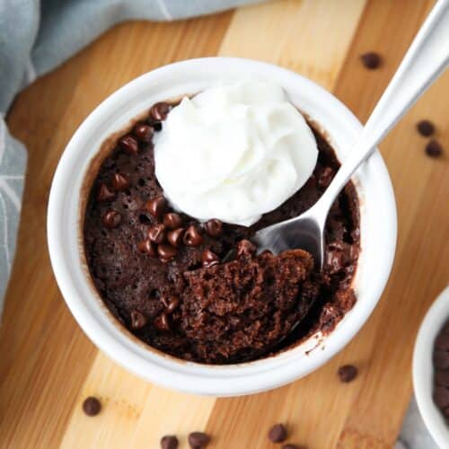 Microwave chocolate cake made in small bowl with chocolate chips and whipped cream on top with a spoonful taken out.