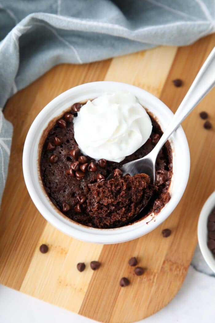 Microwave chocolate cake made in small bowl with chocolate chips and whipped cream on top with a spoonful taken out.