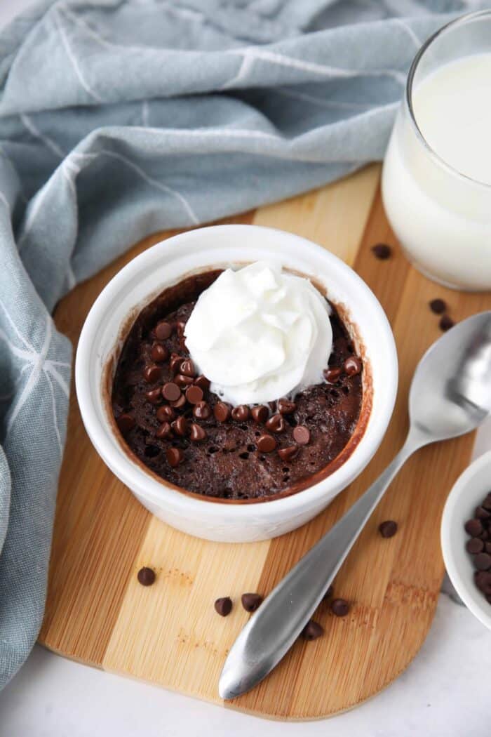 Single serving chocolate cake in a ramekin with mini chocolate chips and whipped on top.