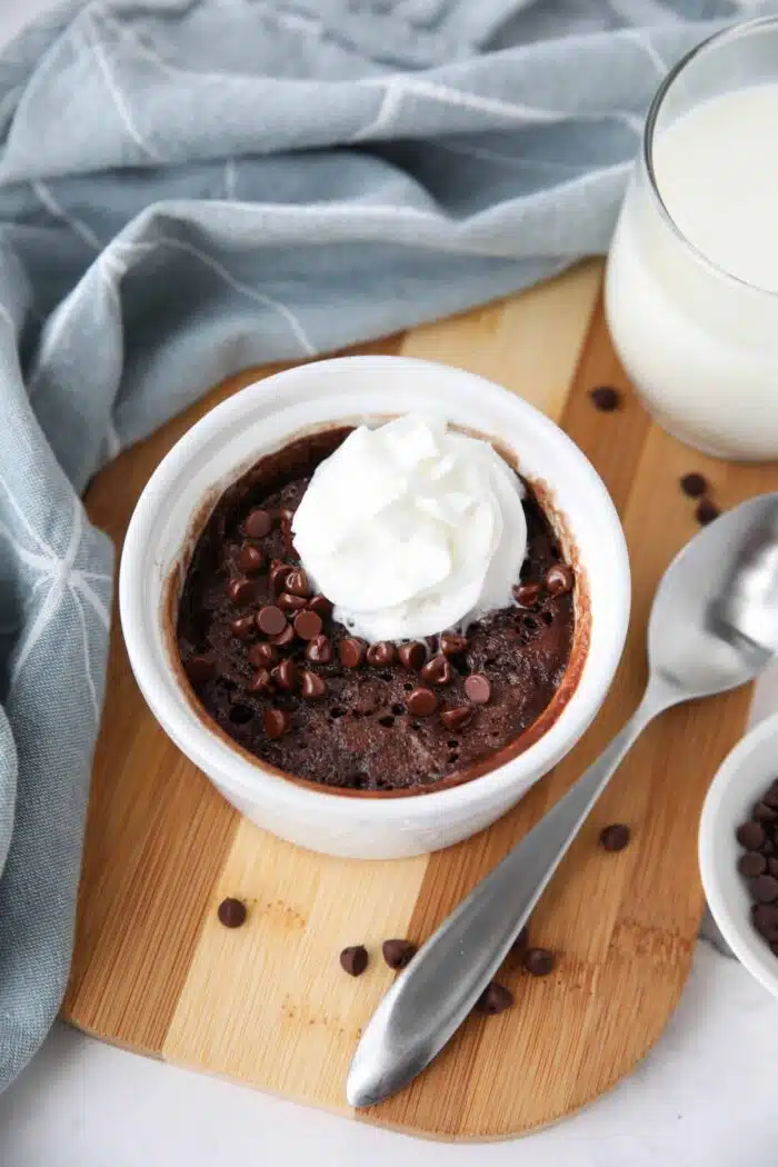 Single serving chocolate cake in a ramekin with mini chocolate chips and whipped on top.