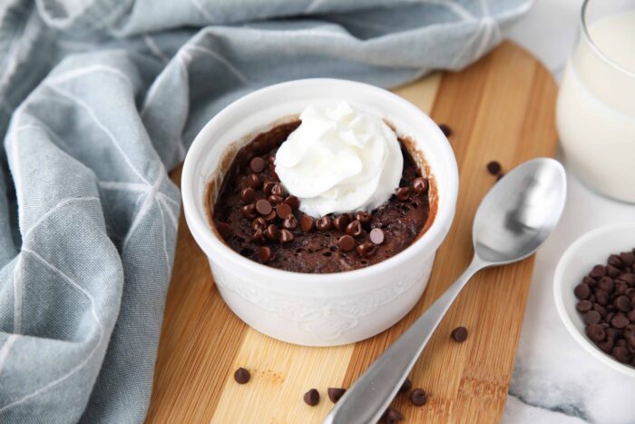 Single serving chocolate cake in a ramekin with mini chocolate chips and whipped on top.