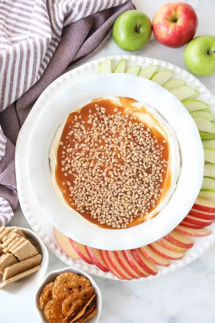 Top view of cream cheese caramel apple dip in a bowl with toffee bits on top and sliced apples on the side.