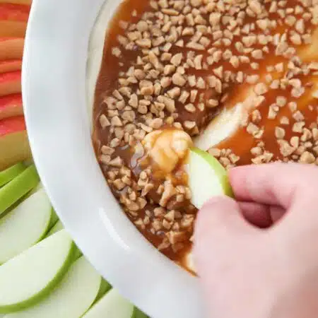 Close up of an apple scooping up cream cheese caramel apple dip.