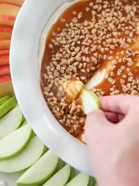 Close up of an apple scooping up cream cheese caramel apple dip.
