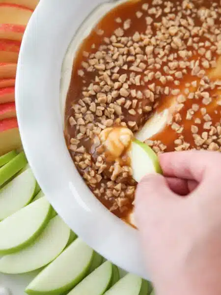 Close up of an apple scooping up cream cheese caramel apple dip.