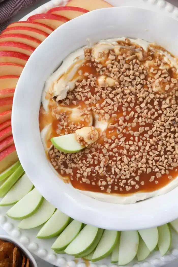 Close up of an apple inside of a bowl full of cream cheese caramel apple dip.