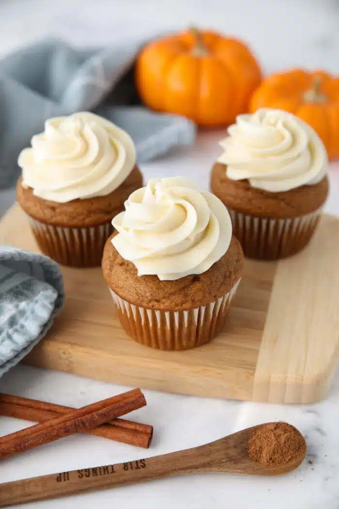Pumpkin cupcakes with cream cheese frosting piped on top sitting on a cutting board.