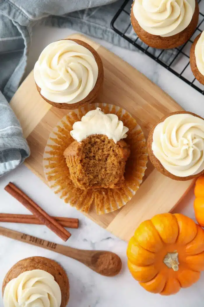 A bite taken out of a pumpkin cupcake with cream cheese frosting.
