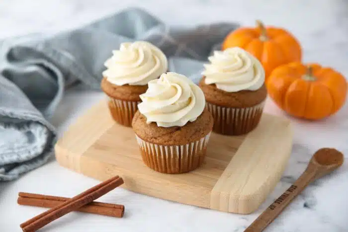 Three pumpkin cupcakes on a cutting board.