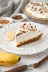 Side view of banoffee pie showing layers of graham cracker crust, dulce de leche, banana slices, whipped cream and toppings.
