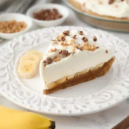 Side view of banoffee pie showing layers of graham cracker crust, dulce de leche, banana slices, whipped cream and toppings.
