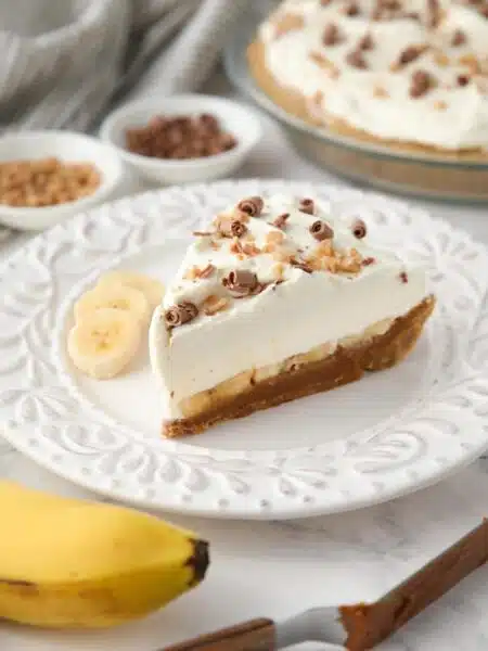 Side view of banoffee pie showing layers of graham cracker crust, dulce de leche, banana slices, whipped cream and toppings.