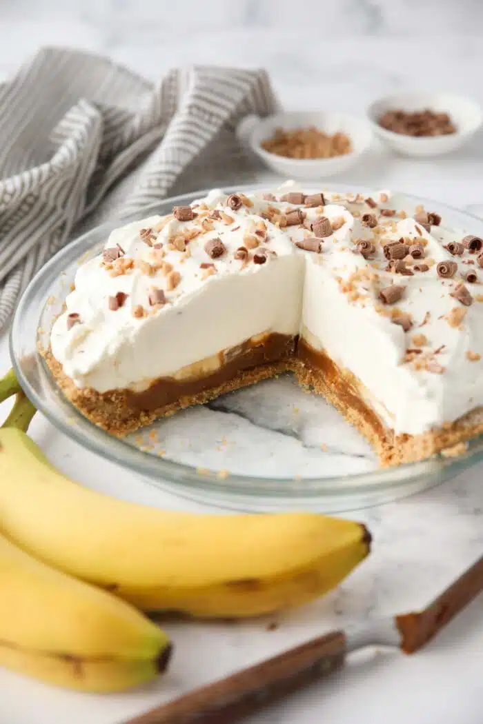 Slices removed from banoffee pie showing layers of graham cracker crust, dulce de leche caramel, bananas, whipped cream and toppings.