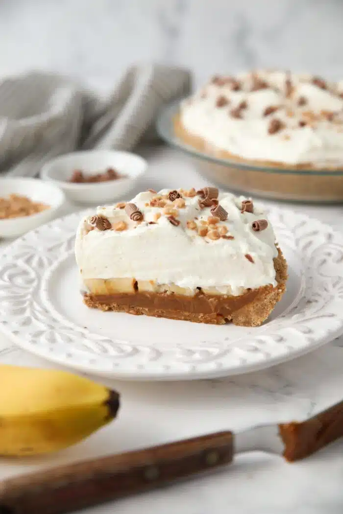 Side view of banoffee pie with graham cracker crust, dulce de leche, and whipped cream topped with toffee bits and chocolate shavings.