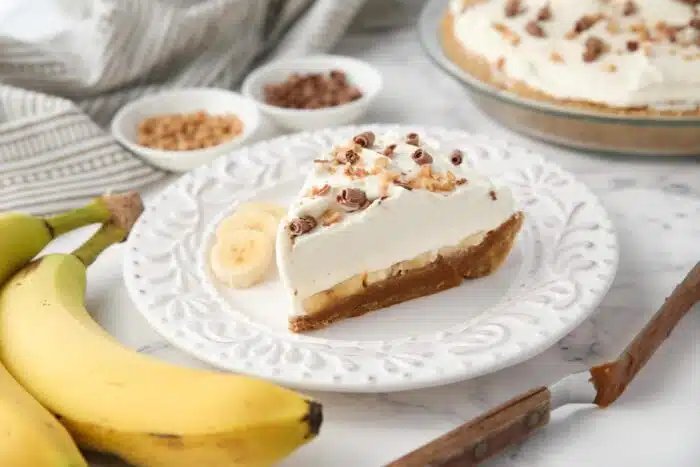 Side view of banoffee pie showing graham cracker crust, dulce de leche, banana slices, whipped cream and toppings.