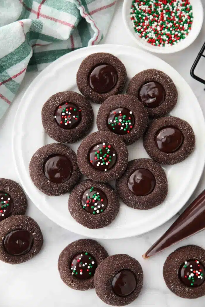 Plate of chocolate thumbprint cookies with ganache centers. Some with holiday sprinkles.