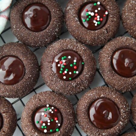Close up of thumbprint chocolate cookies with ganache centers topped with holiday nonpareils.