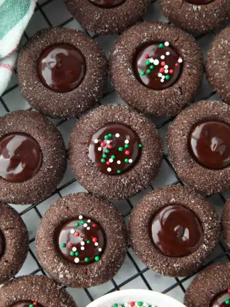 Close up of thumbprint chocolate cookies with ganache centers topped with holiday nonpareils.