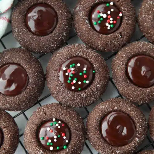 Close up of thumbprint chocolate cookies with ganache centers topped with holiday nonpareils.