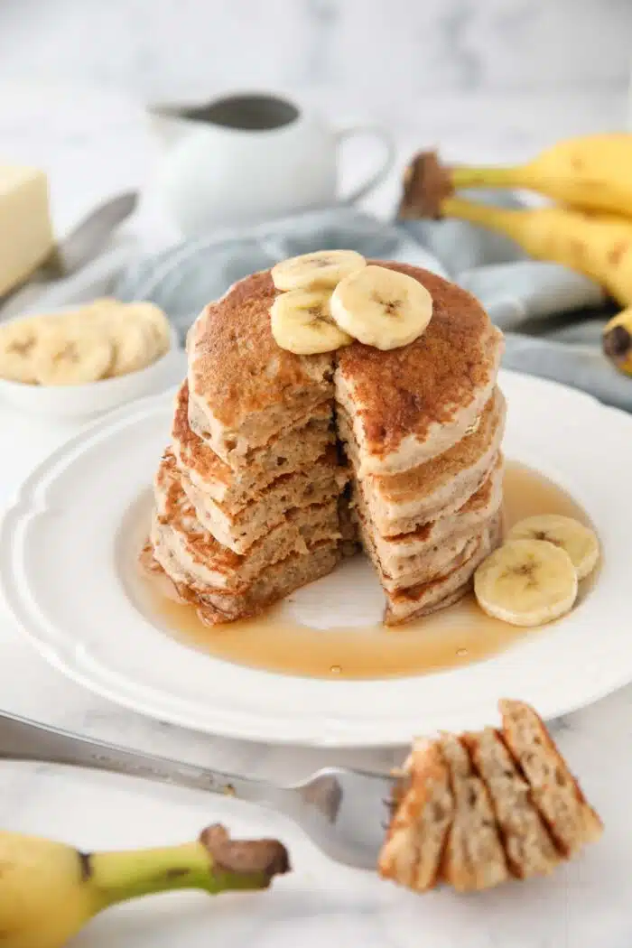 Stack of pancakes with bananas on top and a forkful taken out.
