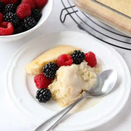 Scoop of homemade vanilla pudding cake on a plate with fresh berries.
