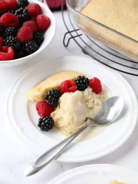 Scoop of homemade vanilla pudding cake on a plate with fresh berries.