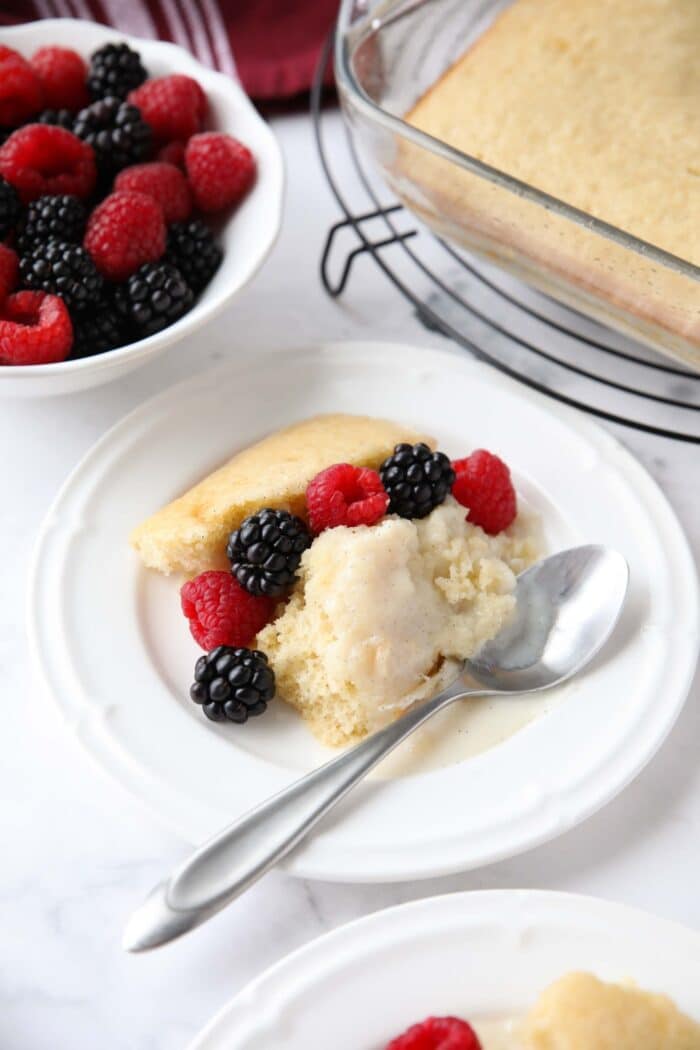 Scoop of homemade vanilla pudding cake on a plate with fresh berries.