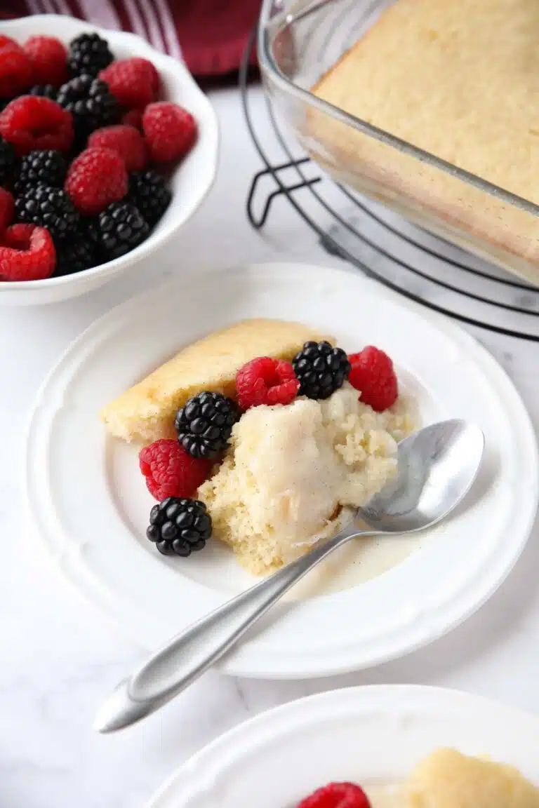 Scoop of homemade vanilla pudding cake on a plate with fresh berries.