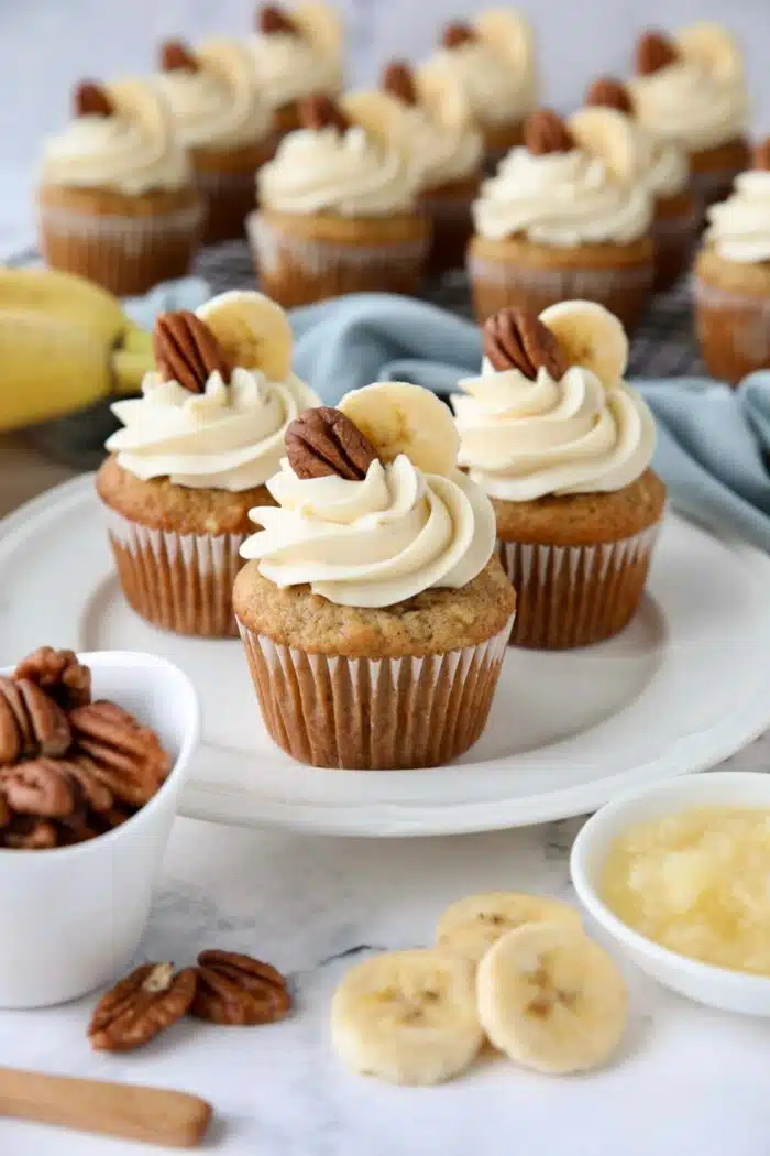 Three hummingbird cupcakes on a plate with cream cheese frosting and a slice of banana and pecan on top.