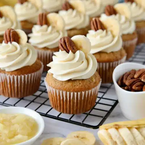 Hummingbird Cupcakes on a wire rack with cream cheese frosting and a slice of banana and pecan on top.
