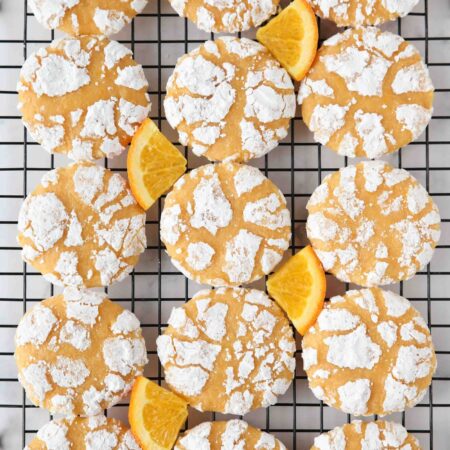 Orange crinkle cookies on a wire cooling rack with orange slices.