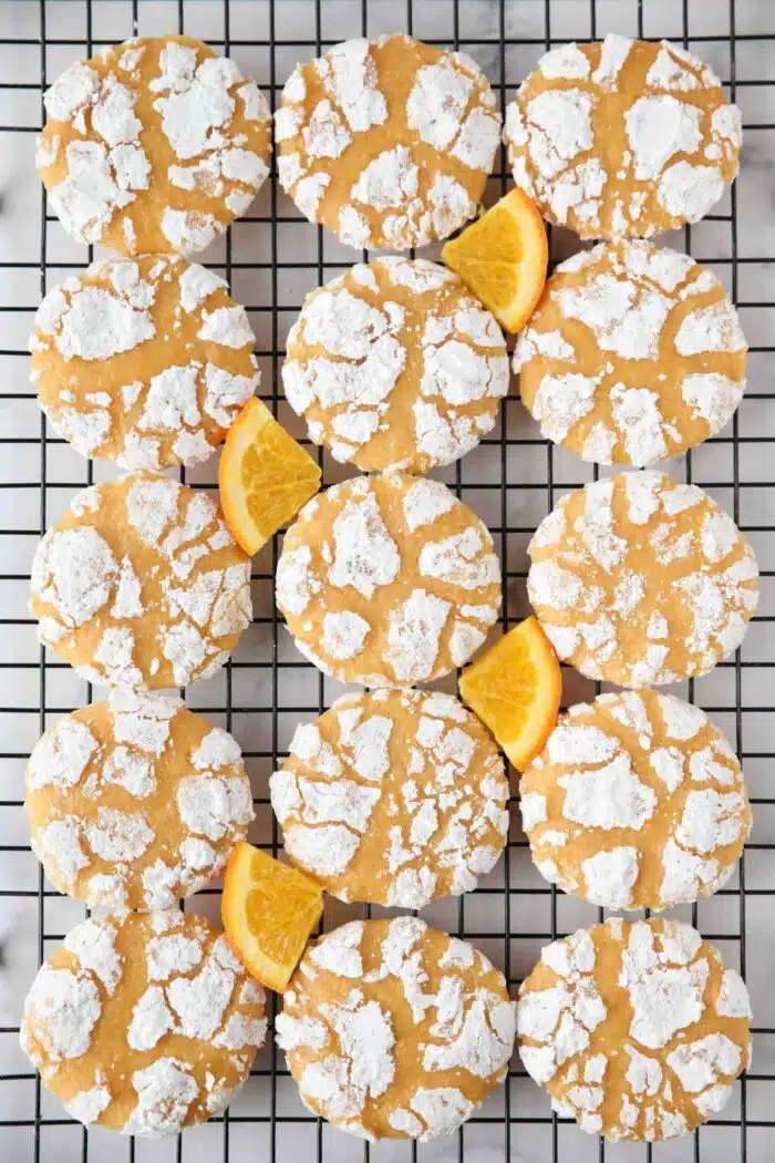 Orange crinkle cookies on a wire cooling rack with orange slices.