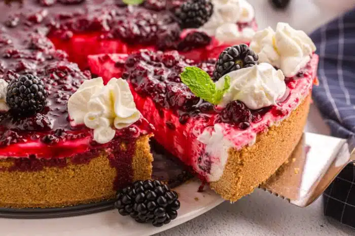 Lifting a slice of no bake summer berry cheesecake from the pan.
