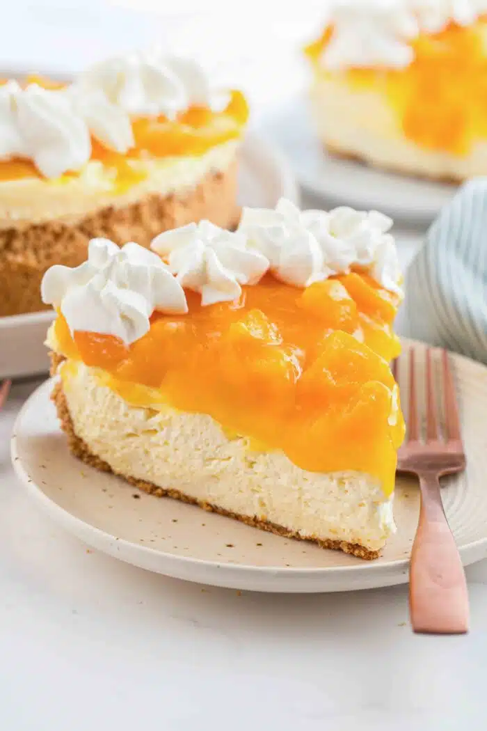 Slice of no bake peach cheesecake on a plate with a fork.