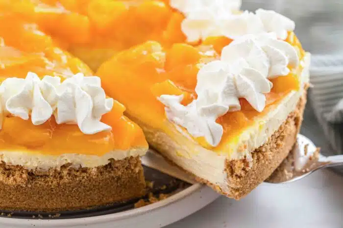 Slice of easy peach cheesecake being lifted from pan.