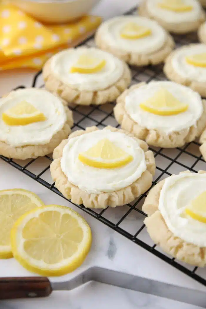 Lemon sugar cookies with lemon frosting and lemon slices on a wire cooling rack.