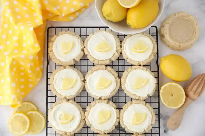 Frosted lemon sugar cookies with lemon slices on a wire cooling rack.