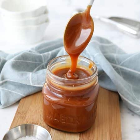 Homemade salted caramel sauce in a jar being drizzled with a spoon.