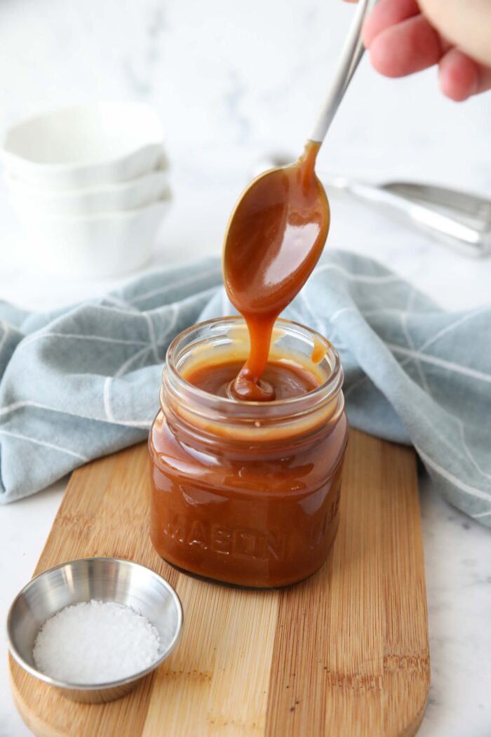 Homemade salted caramel sauce in a jar being drizzled with a spoon.