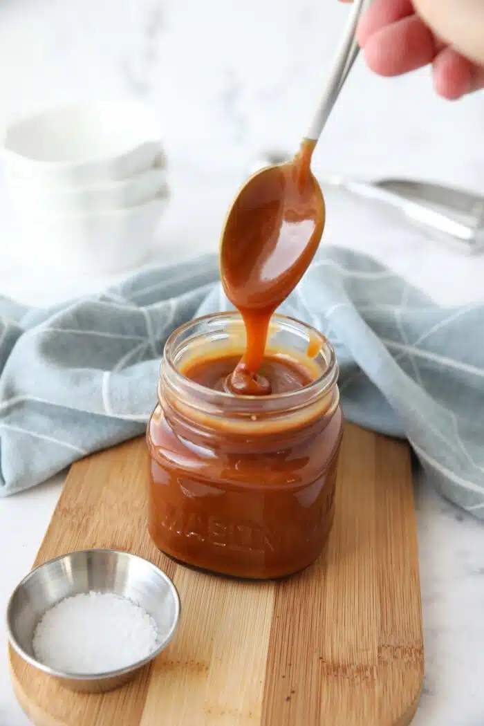 Homemade salted caramel sauce in a jar being drizzled with a spoon.