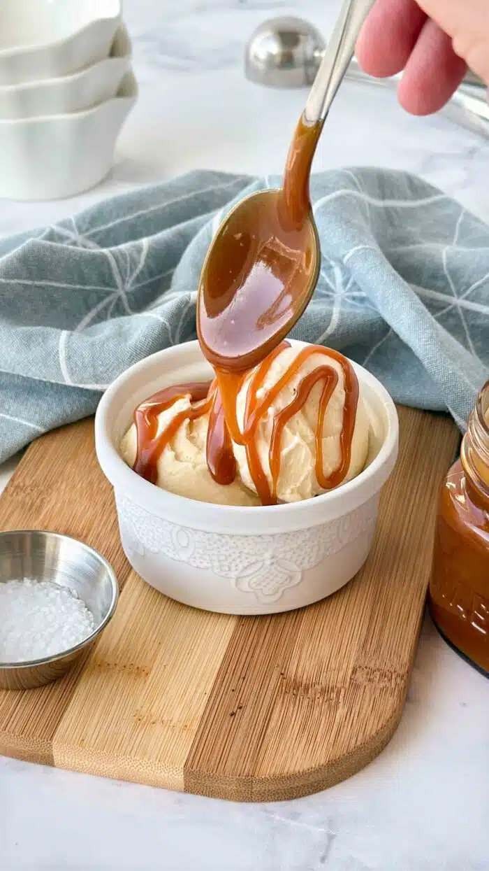 Drizzling salted caramel sauce over ice cream in a bowl.
